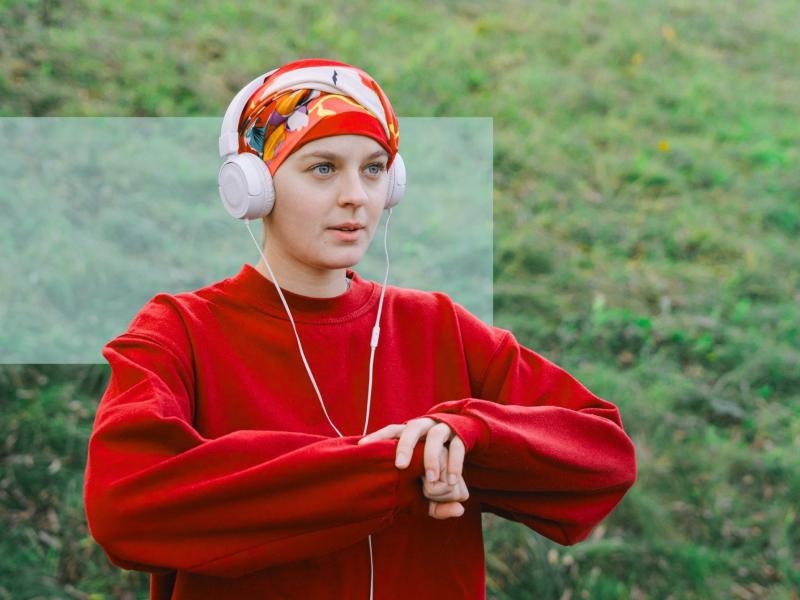 Person i rød sweatshirt og hovedtørklæde lytter til høretelefoner udendørs.